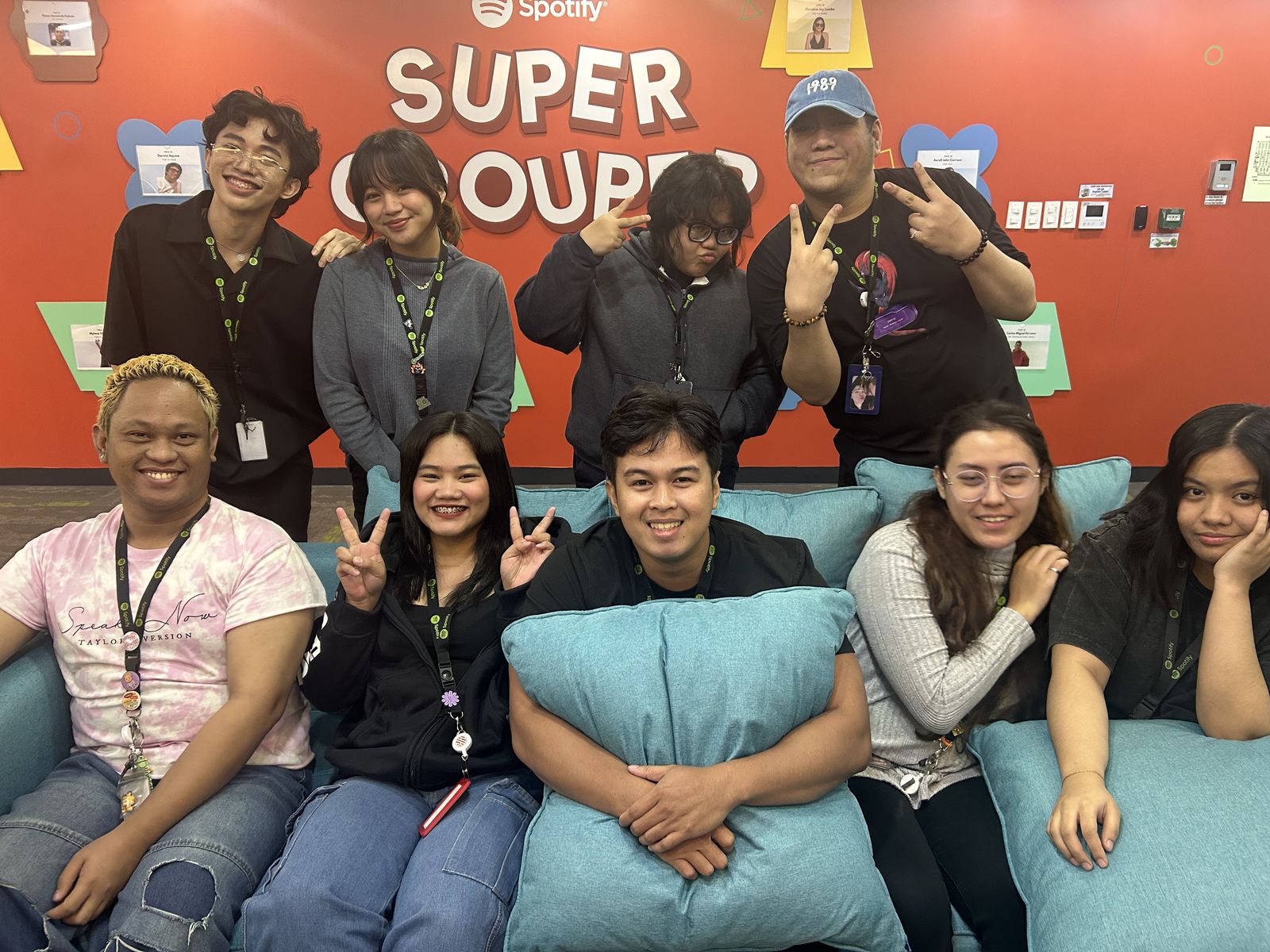 The Wave 101 team at Sutherland Manila, posed on a couch in front of a Spotify wall